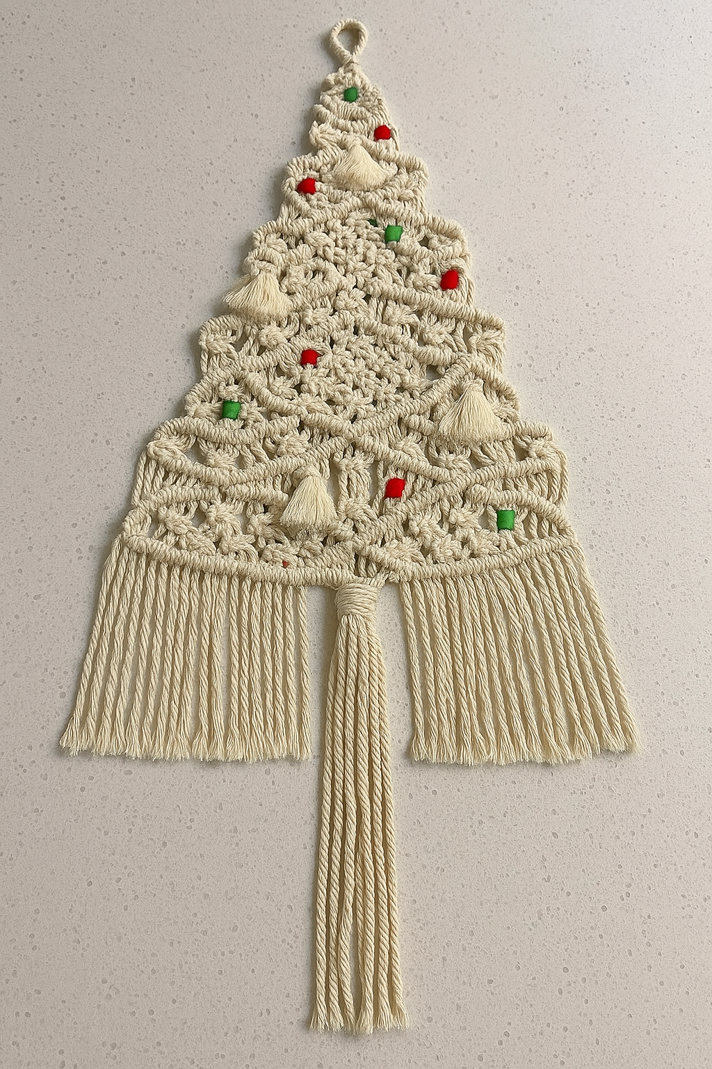 Macrame wall hanging designed like a Christmas tree with decorative elements on a plain background