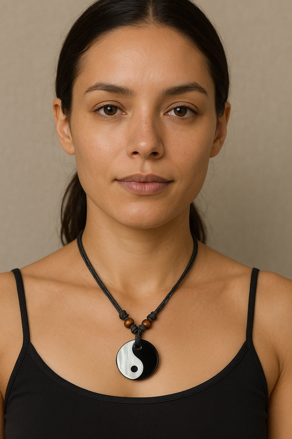 Woman wearing a black tank top and a necklace with a yin yang pendant against a beige background